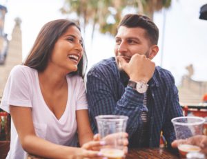man and woman sitting together at a table, drinking drinks and smiling.